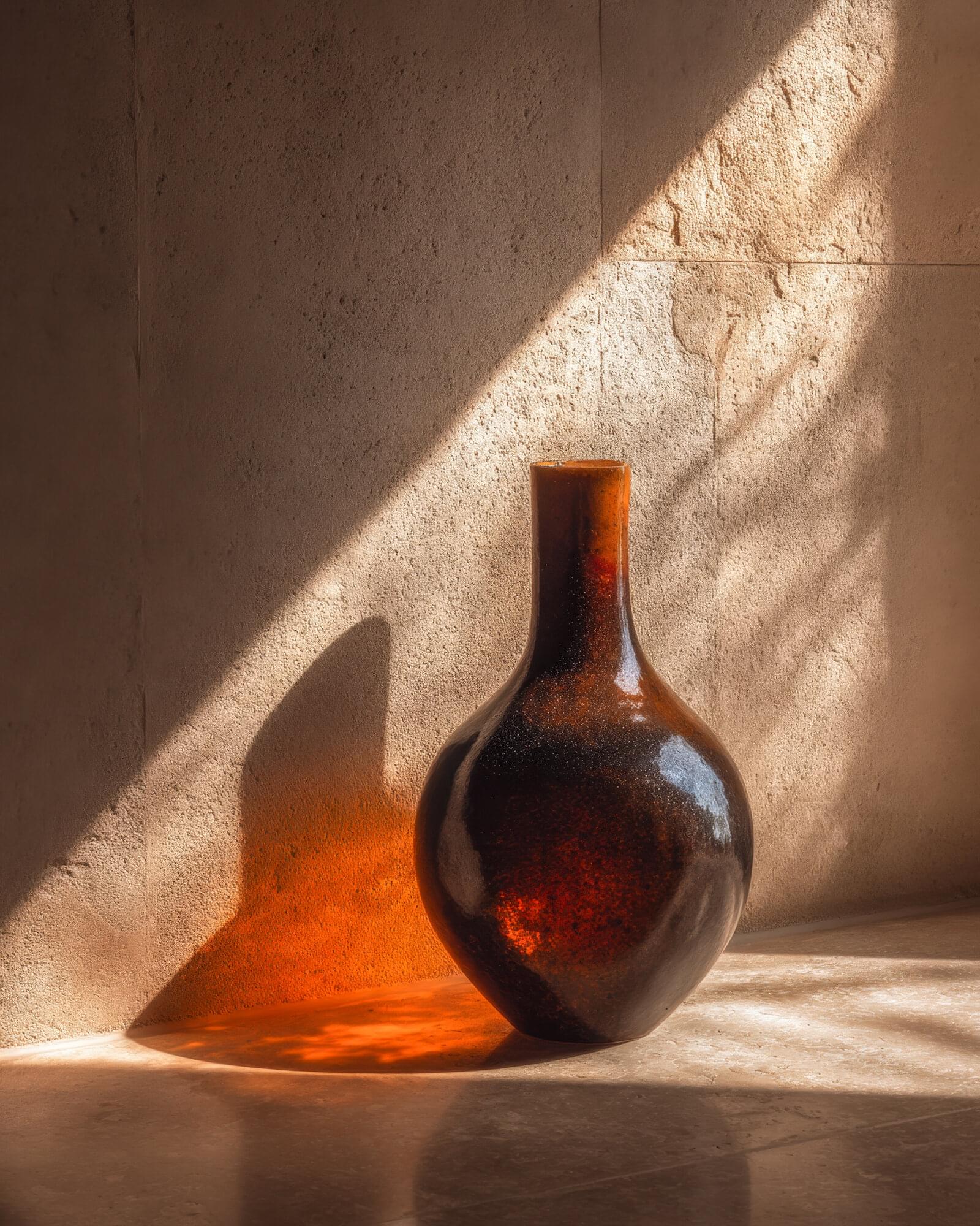 Honey Weight: a dark amber bottle with a narrow neck on a stone floor, raking sunlight turning its shadow to honey.