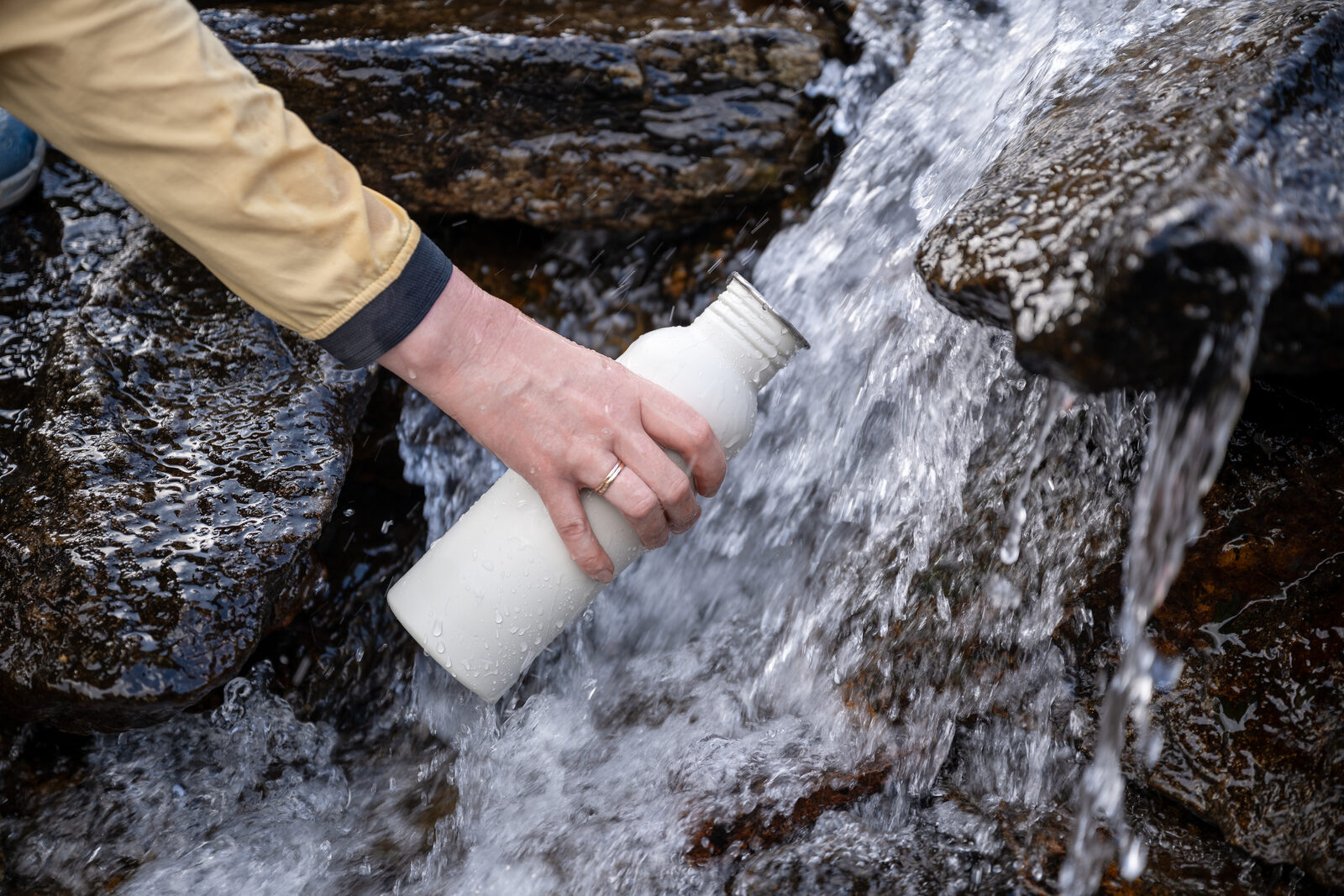 A hand holding a steel bottle under a mountain stream as it fills